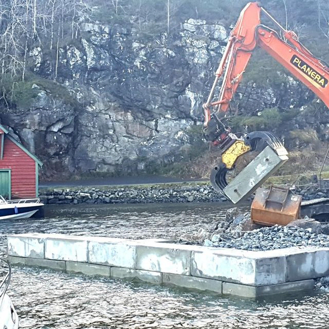 Gravemaskin i arbeid med mur