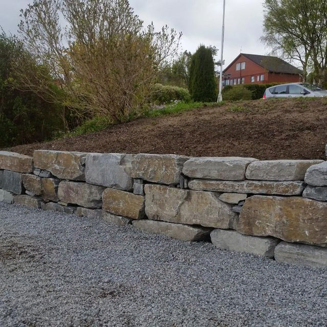 Mur i stor naturstein i innkjørsel med grus